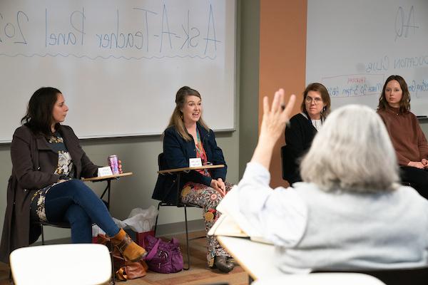 Someone raises their hand to ask a panel of teachers a question